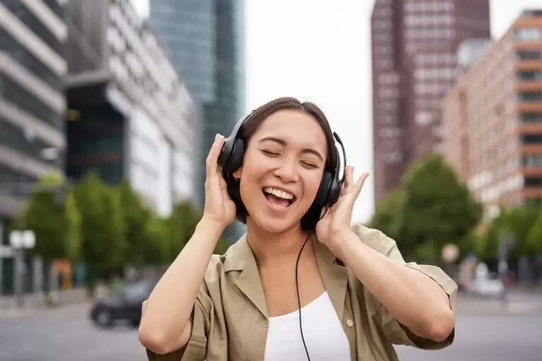 Dancing girl feeling happy in city. Asian woman dancing and listening music in headphones, posing